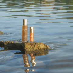 Two bottles of skincare products on a rock with water reflection